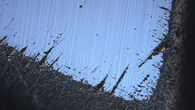 Figure 2. Differential interference contrast image near an apex of the stone showing the roughening of junctions between the faces and evidence of polishing after the roughening occurred. Image by David Fisher; field of view 0.48 mm. Figure 2. Differential interference contrast image near an apex of the stone showing the roughening of junctions between the faces and evidence of polishing after the roughening occurred. Image by David Fisher; field of view 0.48 mm.
