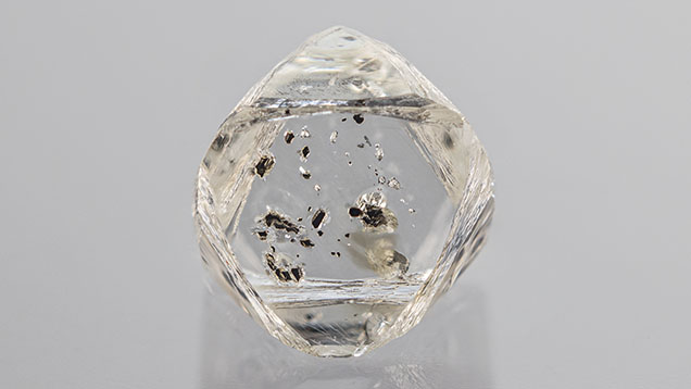 Figure 1. Weighing 1.17 ct and measuring 6.61 mm in the largest dimension, this partially etched colorless diamond octahedron hosts numerous opaque black chromite crystals. Photo by Rhonda Wilson.