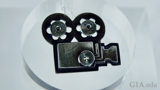 A black sterling silver pendant of a movie camera and film reels.