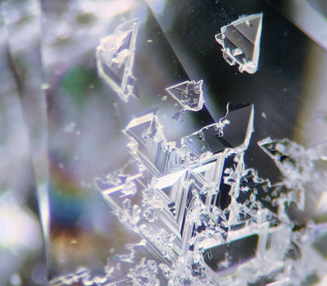 A collection of trigons on the pavilion surface of a round brilliant-cut diamond. Photomicrograph by Isabelle Corvin; field of view approximately 2.0 mm. A collection of trigons on the pavilion surface of a round brilliant-cut diamond. Photomicrograph by Isabelle Corvin; field of view approximately 2.0 mm.