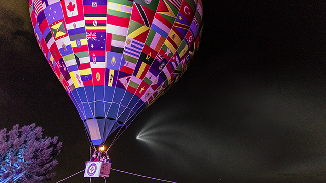 A colorful hot air balloon adorned with various national flags against a dark night sky.