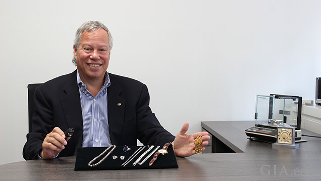 Man sits at his desk with a display stand of multiple pieces of jewelry in front of him. 