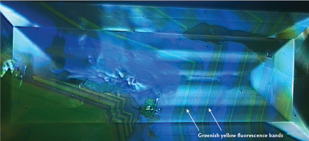 Figure 2. Alternating blue and greenish yellow fluorescence zones were observed with deep-UV excitation. This fluorescence pattern is typical for diamonds colored by the 480 nm visible absorption band. Image by Stephanie Shaw.