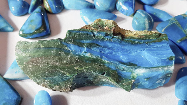 Figure 2. Rough sample of Chilean blue opal, about 18 cm wide, displaying a dull conchoidal fracture, alternating green and blue bands, some white lenses (milky quartz), and a light brown matrix. Photo by Cristiano Brigida; courtesy of Chilean Rocks and Minerals.