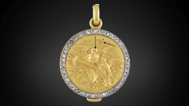 Figure 2. In this gold-plated pendant submitted as 18K solid gold, the base layer tested 10K and the top layer tested 18K. Arrows show where the gold plating has rubbed off due to use. Photo by Diego Sanchez.