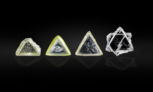 Figure 1. Examples of contact-twinned macle diamond crystals from South Africa. Left to right: a flat triangular macle with limited resorption (sample 11; 0.357 ct); an extensively resorbed variant of a flat triangular macle (sample 12; 0.411 ct); a very elongated flat macle with stacking growth layers on the octahedral faces, showcasing sharp edges and pointed apex corners (sample 13; 0.553 ct); a six-pointed star-shaped, poorly resorbed flat macle (sample 14; 0.747 ct). Photo by Tetsuya Chikayama; courtesy of Suwa & Son, Inc.