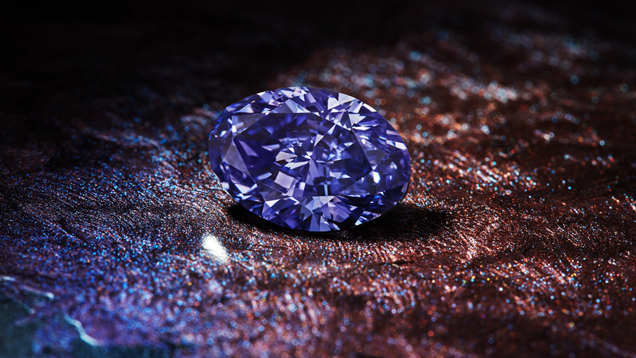 椭圆形的阿盖尔紫罗兰钻石 (Argyle Violet) 展示在带有纹理的棕色、紫色和蓝色表面之上。