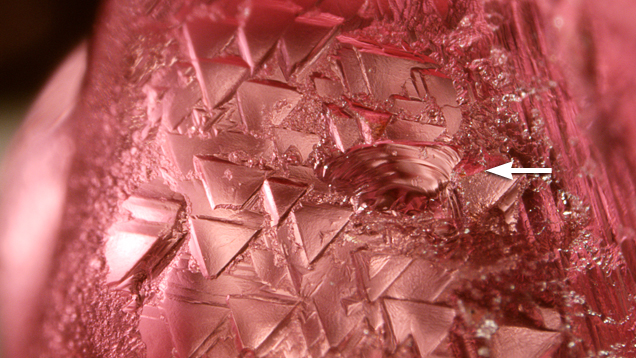 In addition to trigons, the spinel displayed a conchoidal fracture (see arrow), a feature not found in diamond. Magnified 40x. In addition to trigons, the spinel displayed a conchoidal fracture (see arrow), a feature not found in diamond. Magnified 40x.