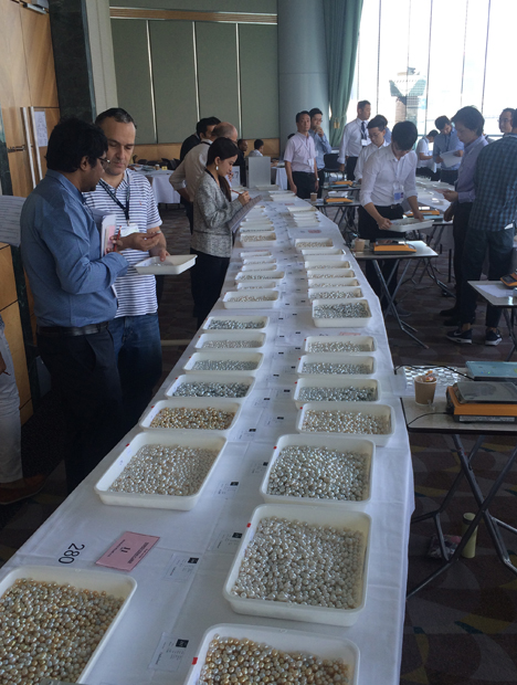 Buyers inspect lot of pearls spread out on long tables. Buyers inspect lot of pearls spread out on long tables.