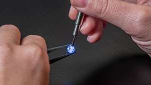 Close up of hands holding a loose stone with tweezers in one hand, and using the iD100 probe to highlight the stone in the other on a black background. 