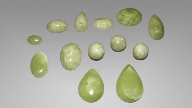 A collection of various green gemstones, including oval and teardrop shapes, displayed against a gray background.