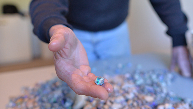 Man showing a piece of rough opal from a pile of stones Man showing a piece of rough opal from a pile of stones