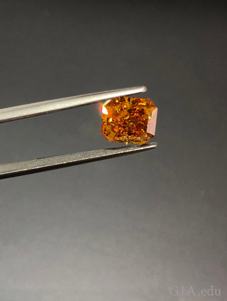 宝石用ピンセットが、オレンジダイヤモンドをつまんでいる。 宝石用ピンセットが、オレンジダイヤモンドをつまんでいる。