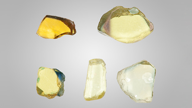Figure 2. A selection of the 102 wafers studied for this report. The three pale yellow wafers are colored by Fe3+ only at a level around 2000 ppma, while the more color-saturated wafer with a blue edge is colored by a much higher concentration of Fe3+ (around 3500 ppma). The deep yellow wafer is colored by Fe3+ and by h•-Fe3+. Photo by John L. Emmett. Figure 2. A selection of the 102 wafers studied for this report. The three pale yellow wafers are colored by Fe3+ only at a level around 2000 ppma, while the more color-saturated wafer with a blue edge is colored by a much higher concentration of Fe3+ (around 3500 ppma). The deep yellow wafer is colored by Fe3+ and by h•-Fe3+. Photo by John L. Emmett.
