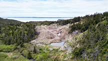alt="Figure 2. View of the amethyst-bearing trench looking west-southwest into Placentia Bay. The vein is exposed in the right side of the trench, and overburden is displaced to the left. Aerial drone photo by Philippe Belley.