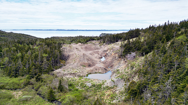 Figure 2. View of the amethyst-bearing trench looking west-southwest into Placentia Bay. The vein is exposed in the right side of the trench, and overburden is displaced to the left. Aerial drone photo by Philippe Belley. Figure 2. View of the amethyst-bearing trench looking west-southwest into Placentia Bay. The vein is exposed in the right side of the trench, and overburden is displaced to the left. Aerial drone photo by Philippe Belley.