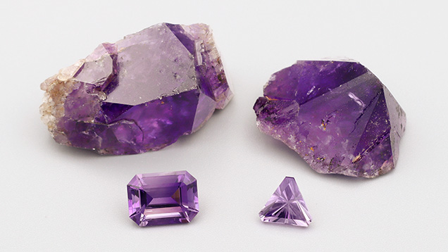 Figure 7. La Manche amethyst rough and faceted stones. The cut stone on the left (5.94 ct) shows diffuse color zoning. The one on the right (2.57 ct) is an example of light purple amethyst. Photo by Philippe Belley. Figure 7. La Manche amethyst rough and faceted stones. The cut stone on the left (5.94 ct) shows diffuse color zoning. The one on the right (2.57 ct) is an example of light purple amethyst. Photo by Philippe Belley.