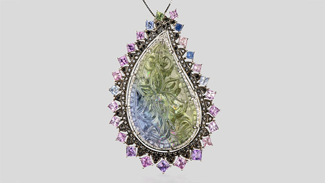 Figure 2. An 18K white gold pendant containing a paisley-shaped unheated tanzanite with a lotus blossom carving, surrounded by pavé-set black diamonds and pink and purple princess-cut Sri Lankan sapphires. The total weight of the diamonds is 1.00 carats, and the colored stones total 23.40 carats. Photo by Robert Weldon; courtesy of YNY Jewels Inc.