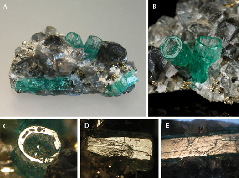 Figure 17. A: In sample 17 (26 mm long), a base of black shale (not visible) is covered with albite, calcite, and pyrite crystals. In this matrix, five emerald crystals are embedded, two of them as deep cups (center) and three as “normal” emeralds (lower right and left). B: Details of the two emerald cups (5.5 mm long on the right). C: In reflected light, the basal plane of one cup appears bright together with the basal faces of small hillocks or columns in the cup. D: Growth steps on the surface of one m prism face of a cup. E: Growth steps on the surface of the m prism face of a “normal” emerald crystal. Photos by K. Schmetzer (A, C–E) and G. Martayan (B); field of view 7.6 mm (C–E). Figure 17. A: In sample 17 (26 mm long), a base of black shale (not visible) is covered with albite, calcite, and pyrite crystals. In this matrix, five emerald crystals are embedded, two of them as deep cups (center) and three as “normal” emeralds (lower right and left). B: Details of the two emerald cups (5.5 mm long on the right). C: In reflected light, the basal plane of one cup appears bright together with the basal faces of small hillocks or columns in the cup. D: Growth steps on the surface of one m prism face of a cup. E: Growth steps on the surface of the m prism face of a “normal” emerald crystal. Photos by K. Schmetzer (A, C–E) and G. Martayan (B); field of view 7.6 mm (C–E).