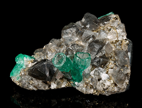Figure 2. In sample 17 (26 mm in length), a base of black shale (not visible) is covered with numerous albite, calcite, and pyrite crystals. In this matrix, five emerald crystals are embedded, two of them developed in the form of empty cups. The emerald cup on the right is 5.5 mm long. Photo by G. Martayan. Figure 2. In sample 17 (26 mm in length), a base of black shale (not visible) is covered with numerous albite, calcite, and pyrite crystals. In this matrix, five emerald crystals are embedded, two of them developed in the form of empty cups. The emerald cup on the right is 5.5 mm long. Photo by G. Martayan.