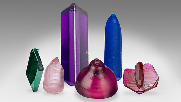 Figure 16. Synthetic crystals from the GIA Museum collection. Left to right: Russian hydrothermal synthetic emerald, flame-fusion pink synthetic spinel, hydrothermal synthetic amethyst with a colorless seed plate, titanium-doped Czochralski-grown purplish pink synthetic sapphire boule, flame-fusion blue synthetic spinel boule, and flux-grown Ramaura synthetic ruby. Photos by Robert Weldon. Figure 16. Synthetic crystals from the GIA Museum collection. Left to right: Russian hydrothermal synthetic emerald, flame-fusion pink synthetic spinel, hydrothermal synthetic amethyst with a colorless seed plate, titanium-doped Czochralski-grown purplish pink synthetic sapphire boule, flame-fusion blue synthetic spinel boule, and flux-grown Ramaura synthetic ruby. Photos by Robert Weldon.