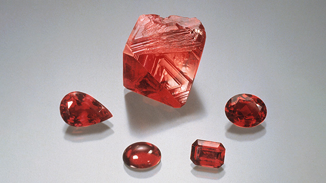 Figure 6. Flux-grown synthetic ruby produced by the Douros method. The rough rhombohedral crystal weighs 44.74 ct, and the cut stones range from 2.14 to 4.93 ct. Photo by Robert Weldon; courtesy of John Douros. Figure 6. Flux-grown synthetic ruby produced by the Douros method. The rough rhombohedral crystal weighs 44.74 ct, and the cut stones range from 2.14 to 4.93 ct. Photo by Robert Weldon; courtesy of John Douros.