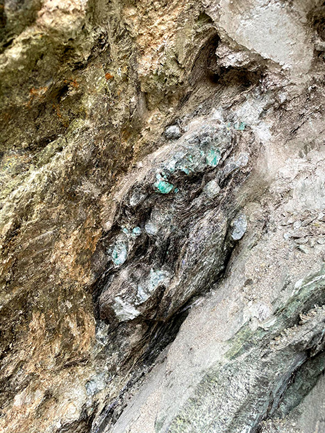 Figure 2. An emerald pocket at the reaction zone between the pale pegmatite intrusion (bottom right) and ultramafic greenish rock (top left). The emeralds are encrusted in dark mica crystals. Photo by Matthew Allen; field of view approximately 50 cm.