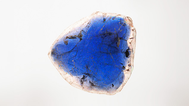 Figure 3. Viewed in immersion, the flux-grown sapphire crystal exhibited strong color zoning, with a deep blue center and a rim that appeared colorless. Photo by Gagan Choudhary. Figure 3. Viewed in immersion, the flux-grown sapphire crystal exhibited strong color zoning, with a deep blue center and a rim that appeared colorless. Photo by Gagan Choudhary.
