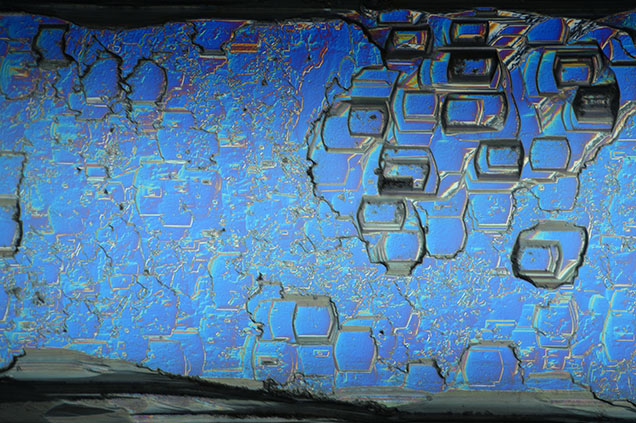 Figure 3. Aquamarine viewed with differential interference contrast filters. Hexagonal, pseudorectangular, and uneven etch features exist on every prismatic face and run the length of the crystal. Photomicrograph by Rhiana Henry; field of view 2.88 mm. Figure 3. Aquamarine viewed with differential interference contrast filters. Hexagonal, pseudorectangular, and uneven etch features exist on every prismatic face and run the length of the crystal. Photomicrograph by Rhiana Henry; field of view 2.88 mm.