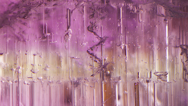This pink tourmaline from Brazil shows color zoning and numerous growth blockages. An interesting spiral dislocation is also seen parallel to the c-axis of the crystal. Field of view 2.21 mm. This pink tourmaline from Brazil shows color zoning and numerous growth blockages. An interesting spiral dislocation is also seen parallel to the c-axis of the crystal. Field of view 2.21 mm.