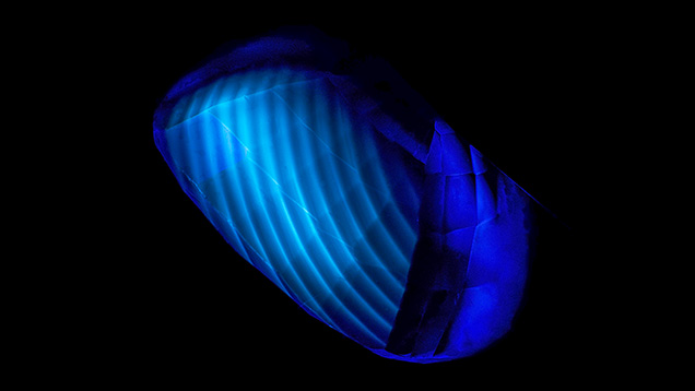 Figure 11. The curved banding in this flame-fusion synthetic blue sapphire is revealed by deep-UV illumination. From Hughes (2019); field of view ~13 mm. Figure 11. The curved banding in this flame-fusion synthetic blue sapphire is revealed by deep-UV illumination. From Hughes (2019); field of view ~13 mm.