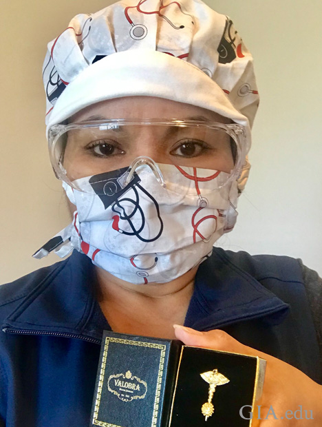 一名带着护目镜和口罩的护士，手持一个装有抗击新冠病毒别针的盒子。