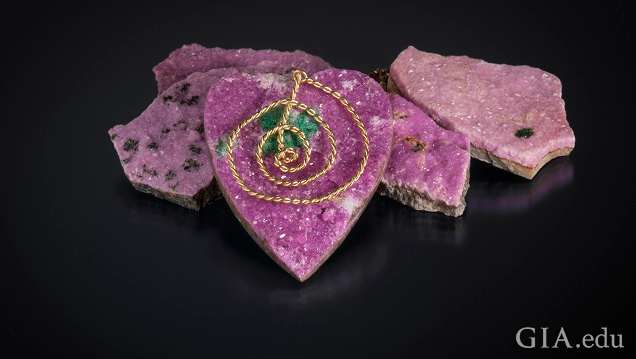A heart-shaped piece of pink drusy hangs from a gold chain. A heart-shaped piece of pink drusy hangs from a gold chain.