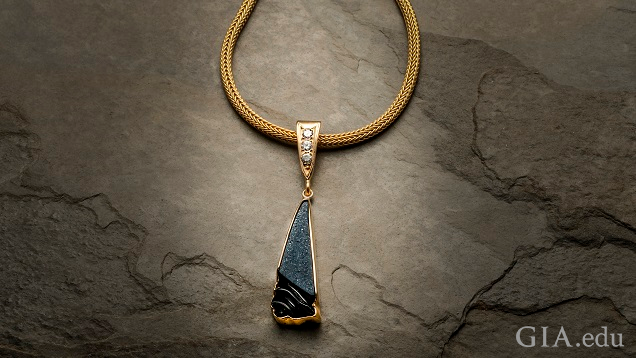 A triangle-shaped piece of black onyx drusy carving is framed in 14k yellow gold. It hangs from a triangle-shaped gold bail set with three 0.10 pt diamonds on a gold chain. A triangle-shaped piece of black onyx drusy carving is framed in 14k yellow gold. It hangs from a triangle-shaped gold bail set with three 0.10 pt diamonds on a gold chain.