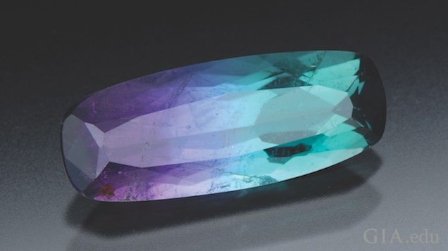 An elongated rectangular cut tourmaline displays shades of purple and tourquoise. An elongated rectangular cut tourmaline displays shades of purple and tourquoise.
