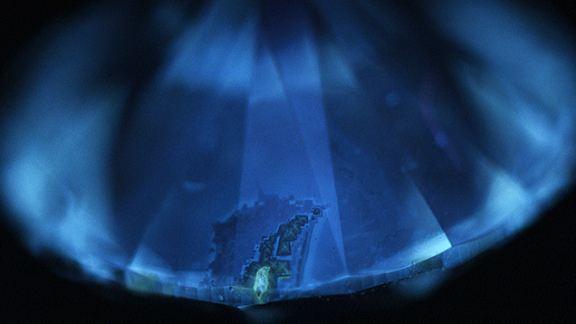 Figure 3. When exposed to deep-UV excitation, the bulk of the diamond showed blue surface fluorescence, whereas the yellow color zones and the cross patterns with visibly darker particles showed weak yellow surface fluorescence. Image by Sally Eaton-Magaña. Figure 3. When exposed to deep-UV excitation, the bulk of the diamond showed blue surface fluorescence, whereas the yellow color zones and the cross patterns with visibly darker particles showed weak yellow surface fluorescence. Image by Sally Eaton-Magaña.